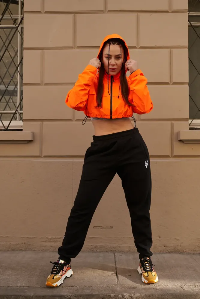 Editorial streetwear: cortaviento naranjo sobre fachada beige