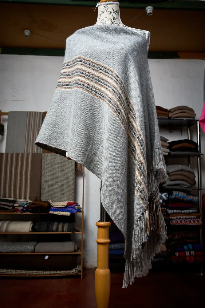 Poncho de alpaca gris con franjas en tonos tierra, sobre maniquí