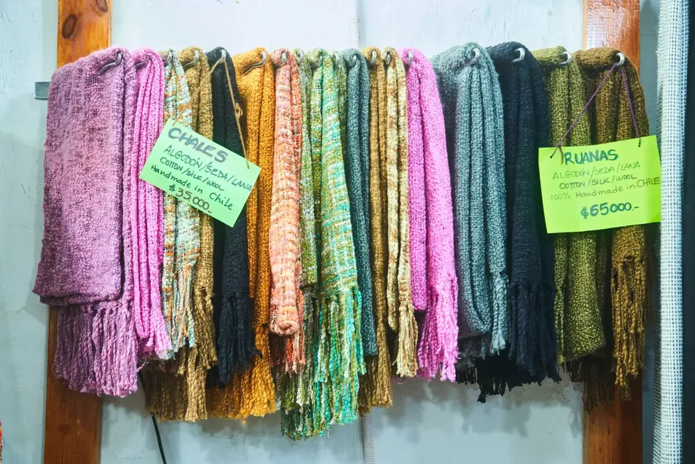 Pared de chales de colores con precios escritos a mano en tienda textil